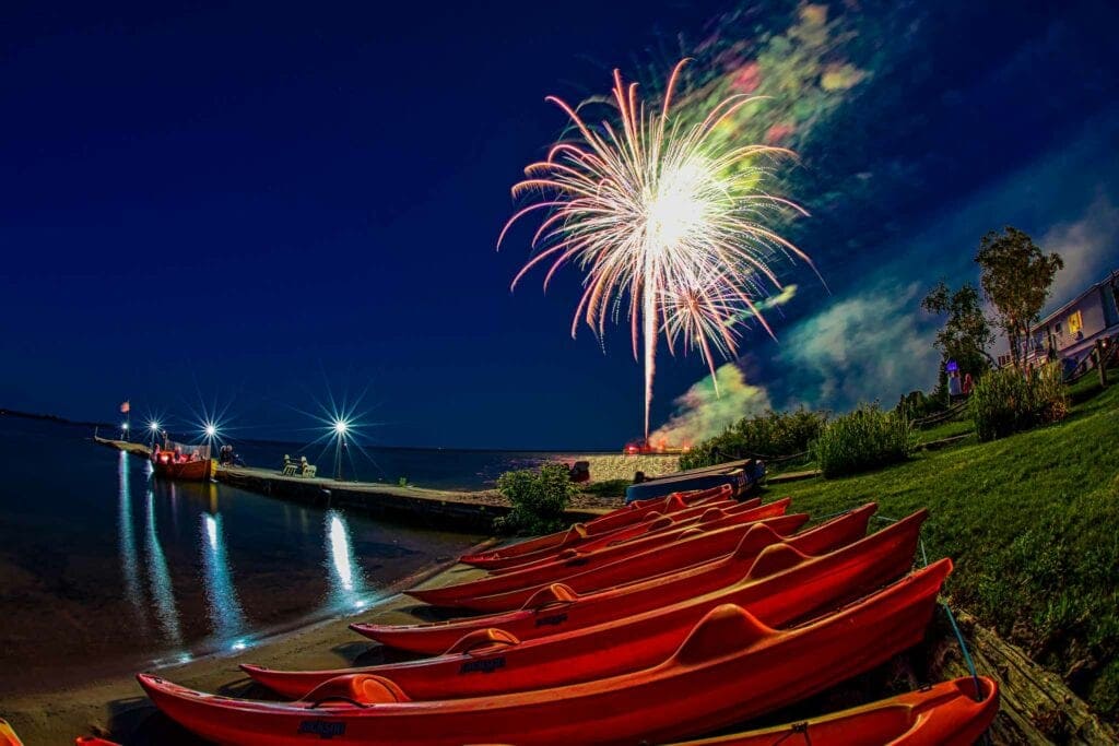 Red kayaks lined up on the shore under fireworks at night, Door County
