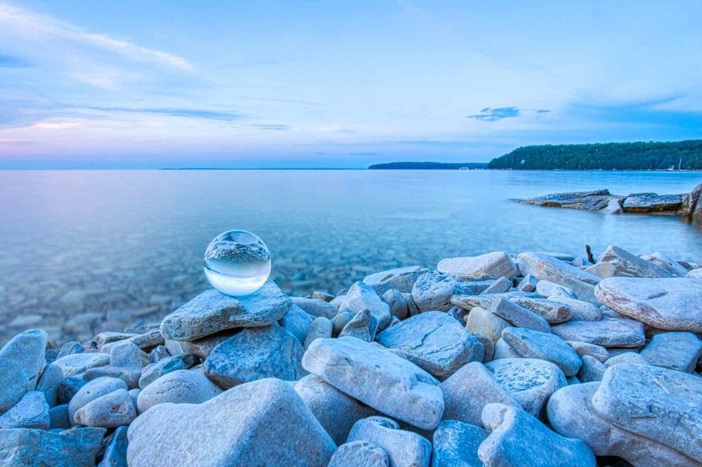 A crystal sphere resting on the smooth gray rocks of Garrett Bay at dusk, calm water beyond