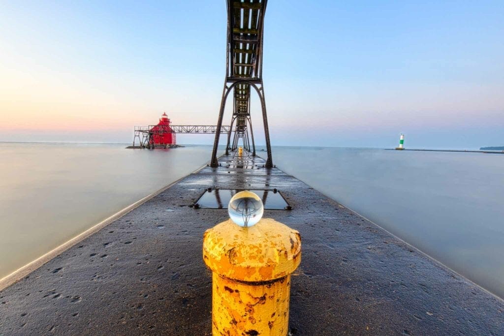 A yellow mooring post on the Sturgeon Bay pier at sunrise, the red light beyond