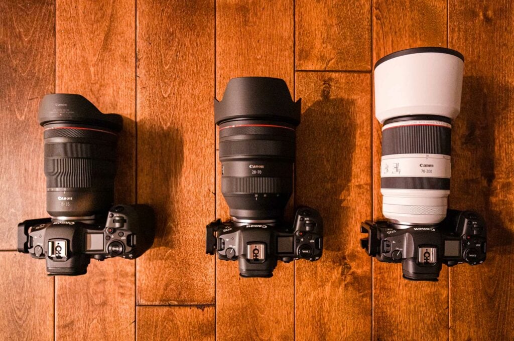 Three Canon RF lenses mounted on camera bodies on a wooden floor