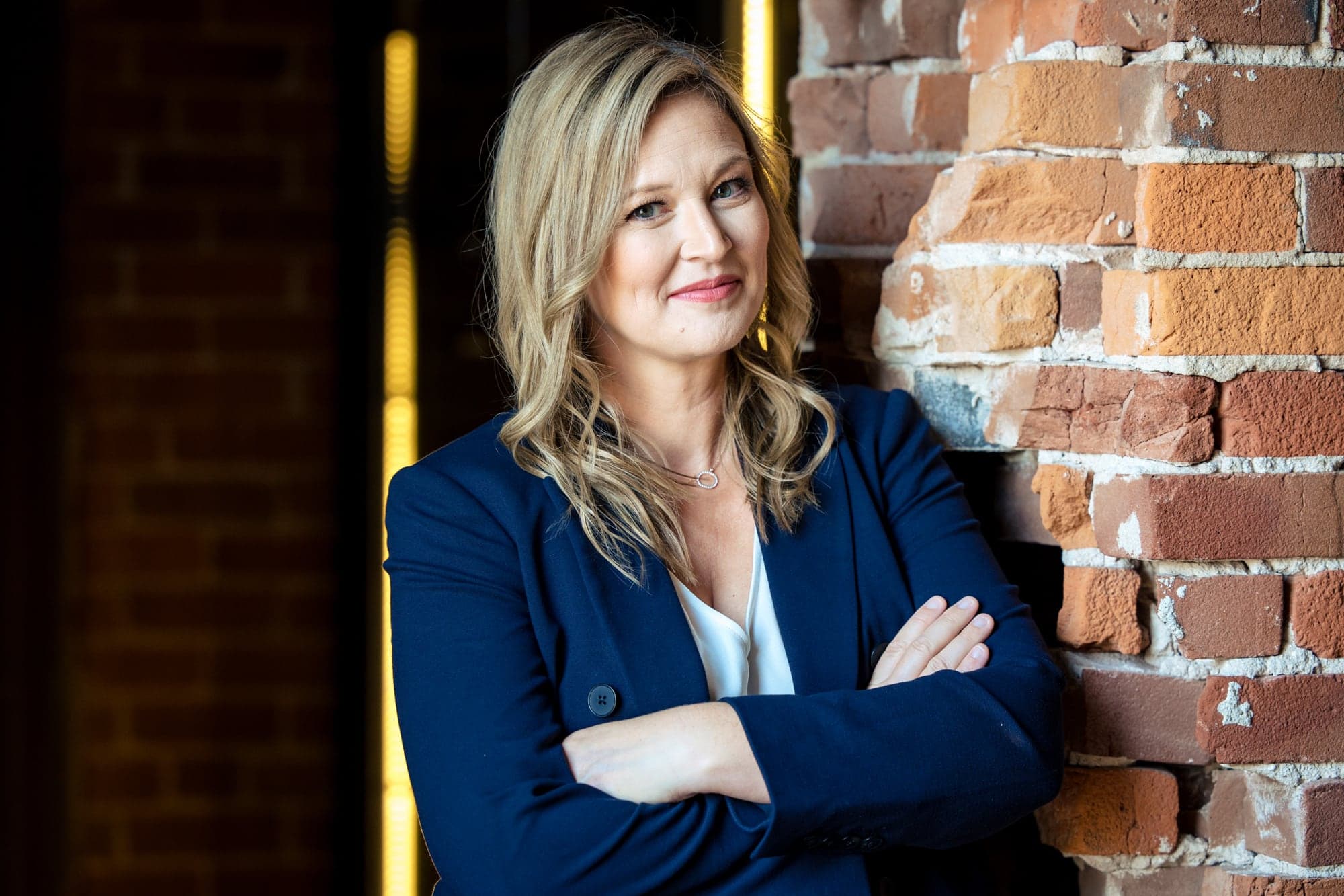 Arms crossed against an exposed brick wall in a navy blazer