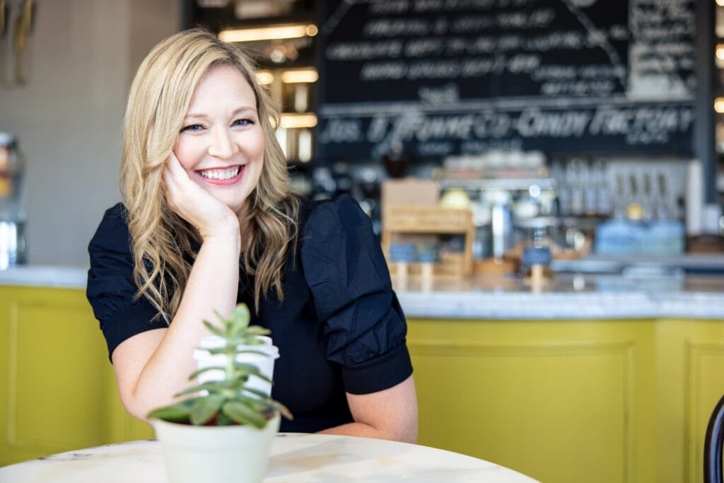 Smiling woman in black shirt at café counter with small succulent plant, natural light