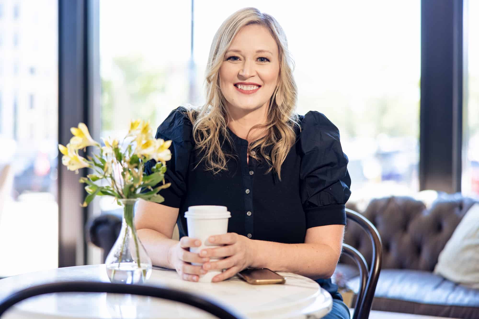 Holding a coffee cup at a table of yellow flowers