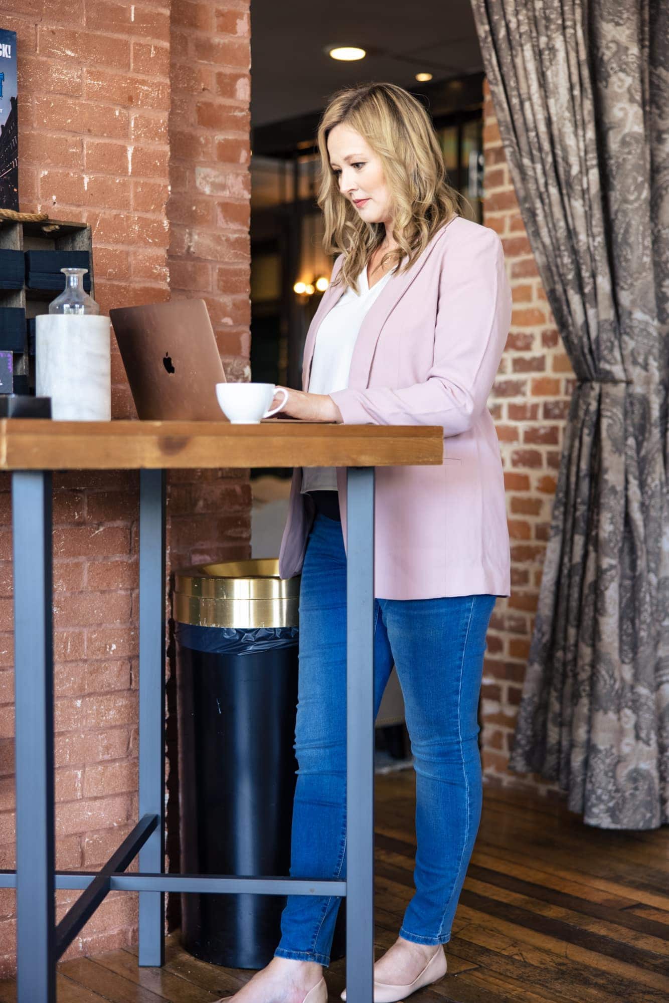 Standing at a bar-height desk with a laptop and coffee, full length