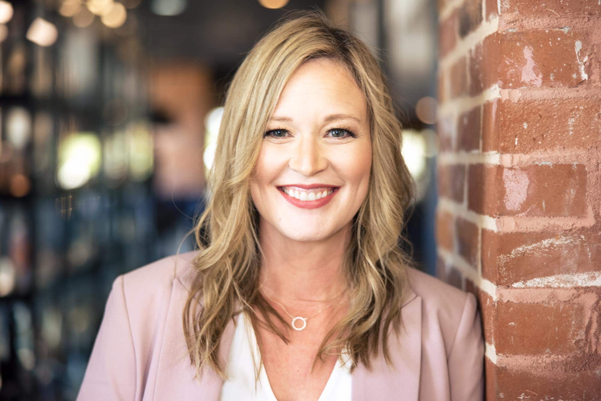 Warm mid-length frame against brick in a blush blazer