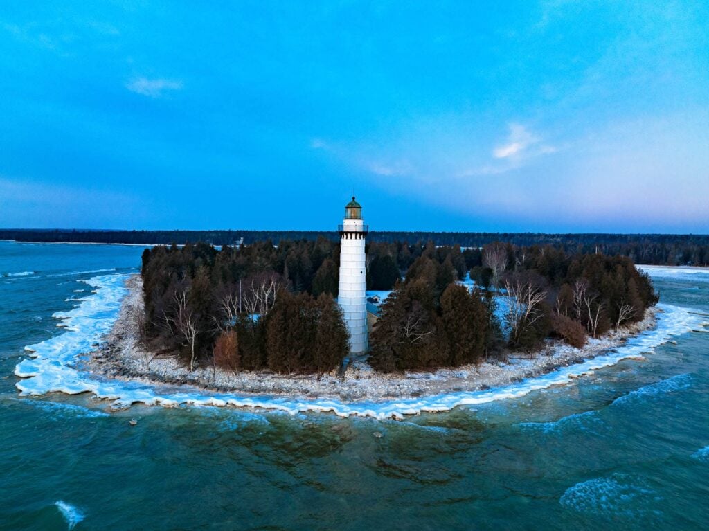 The white Cana Island lighthouse on its wooded island, turquoise water and ice around it