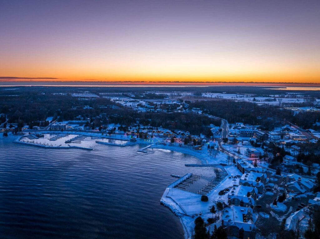 Frozen Door County shoreline at sunrise, with snow-covered buildings and docks along the water's edge under purple and gold sky