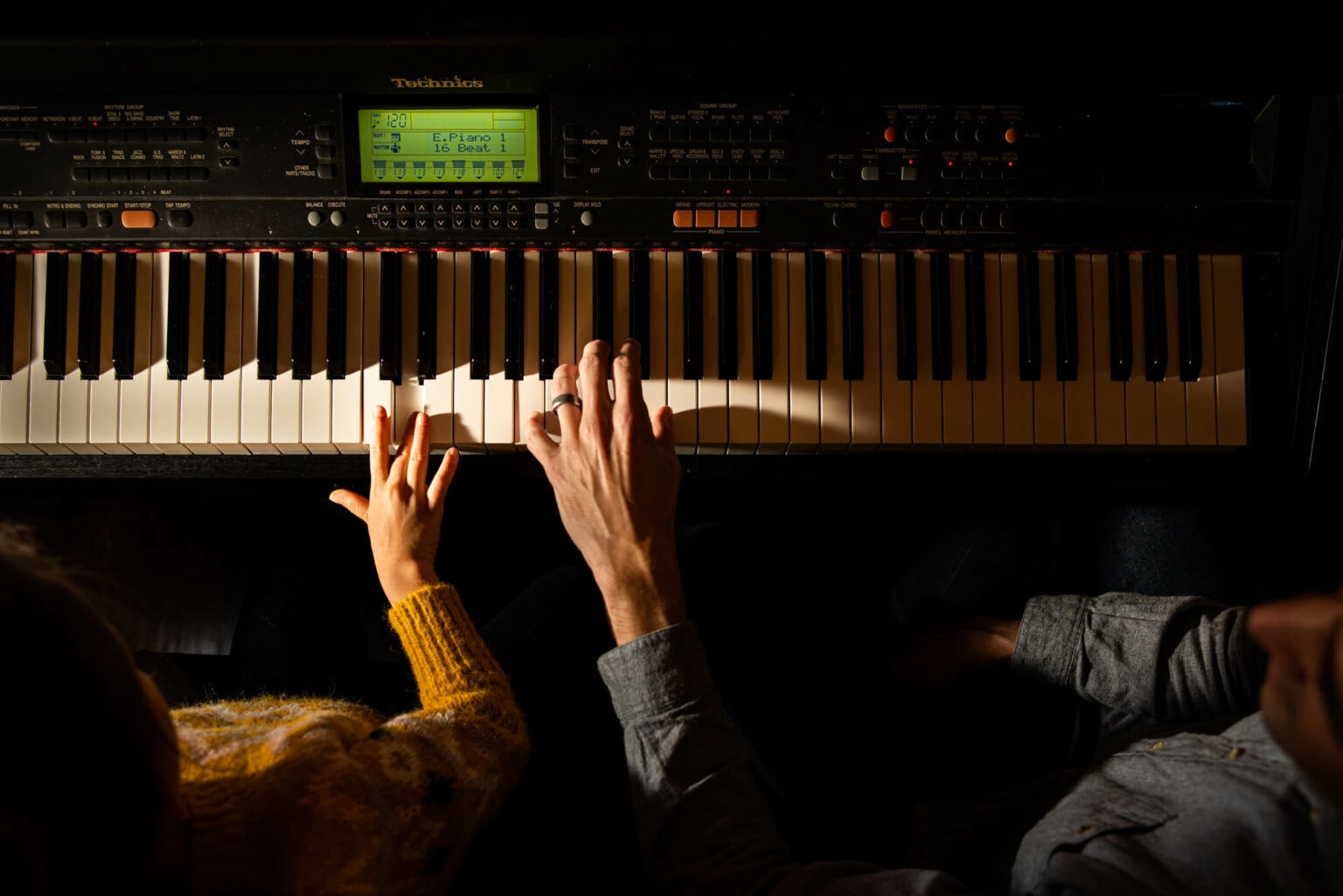 Two musicians’ hands on an illuminated keyboard