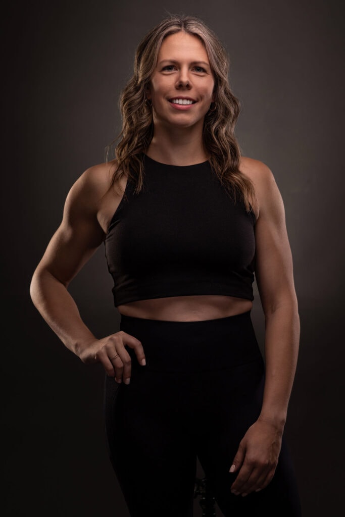 Woman in black crop top and leggings poses against dark background in fitness portrait session
