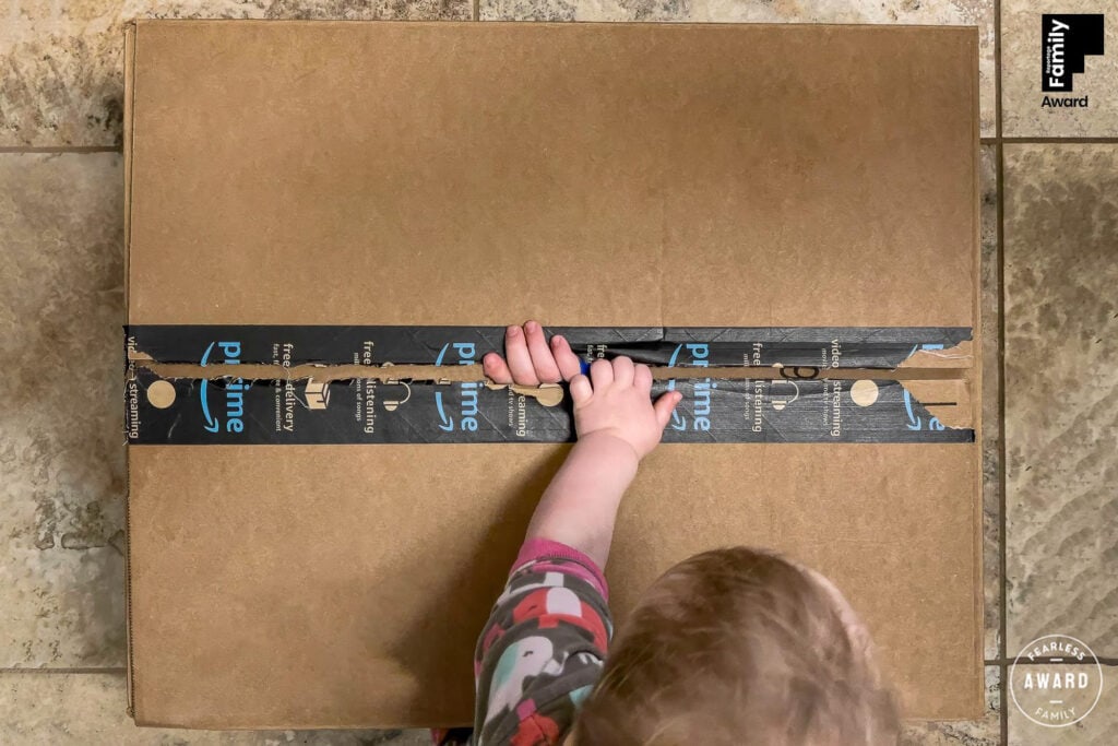 Child's hand pointing at blue circuit board design on cardboard box, overhead view