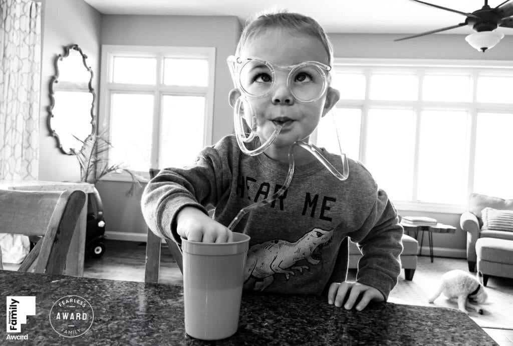 Toddler in glasses playing with string at kitchen counter, black and white family portrait