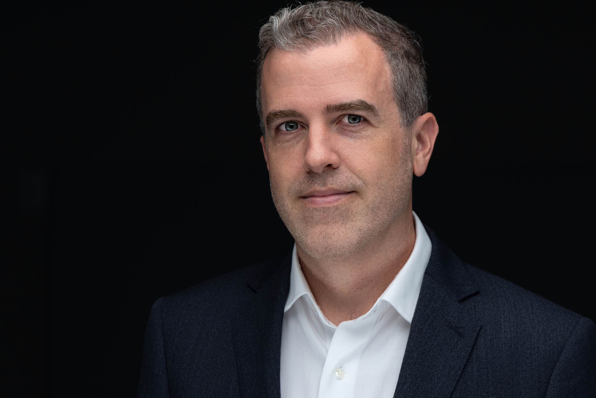 Headshot of a man in a dark blazer against a black backdrop
