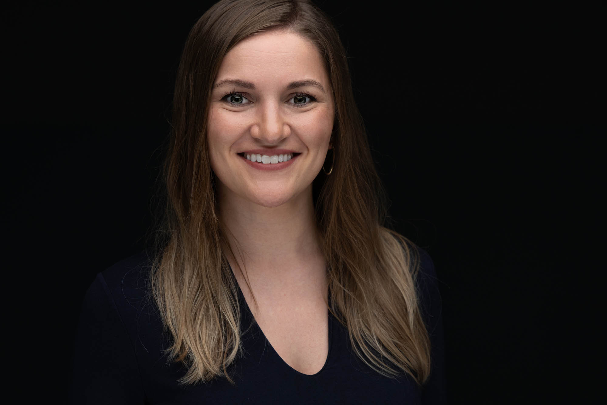 Headshot of a woman in a dark V-neck against a black backdrop