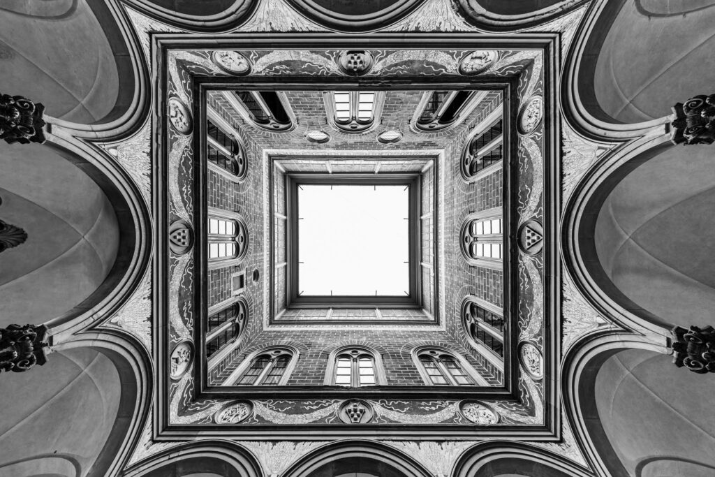 Symmetrical view upward through ornate architectural ceiling with nested square frames and bright skylight, Florence or London