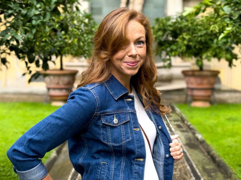 Woman in denim jacket smiling at camera in lush garden courtyard, Florence, Italy