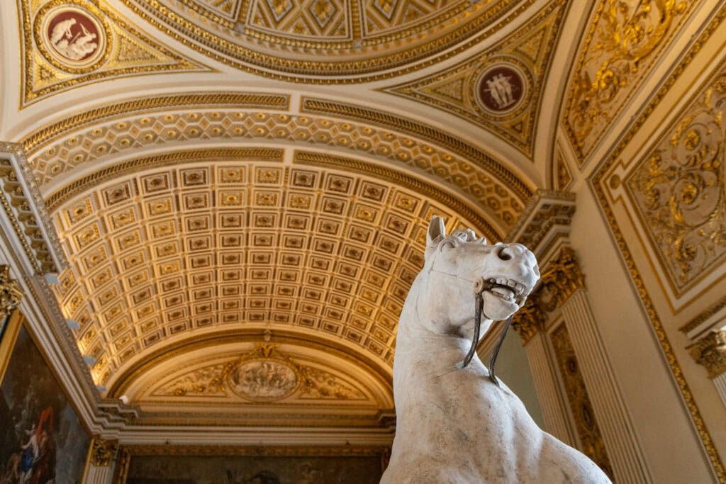 A white marble horse statue beneath a gilded ceiling, Florence