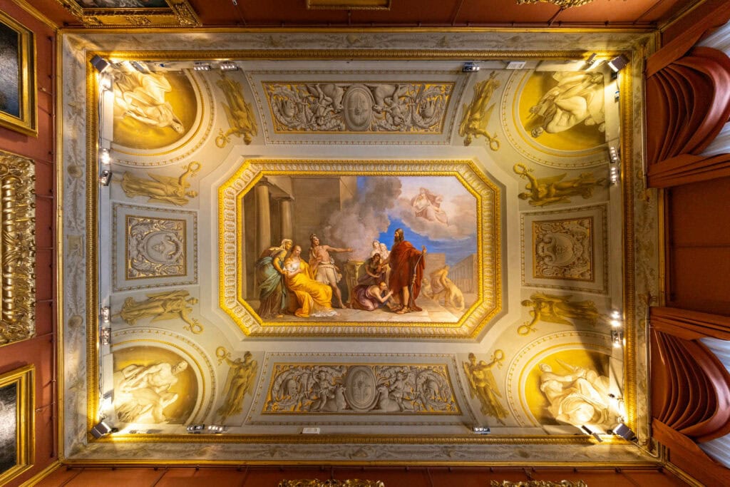 Ornate Baroque ceiling with gilded details, classical sculptures, and central religious fresco in warm golden light, Florence, Italy