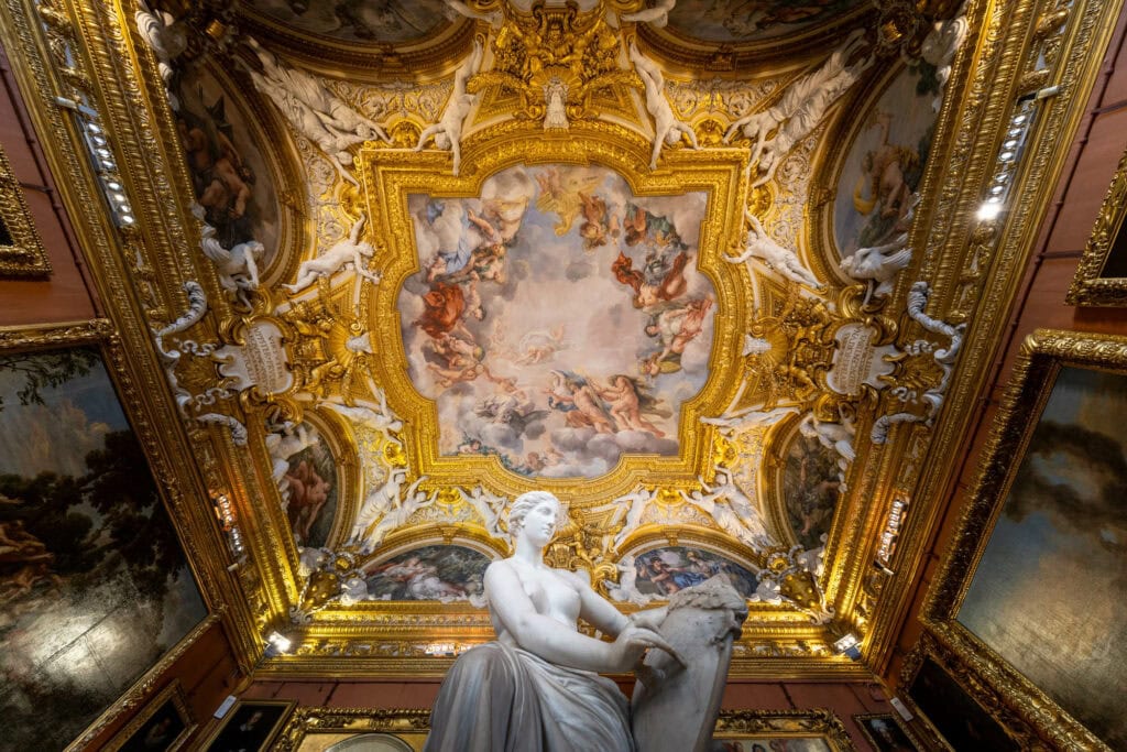 White marble statue beneath ornate gilded ceiling with Renaissance frescoes, Florence, Italy
