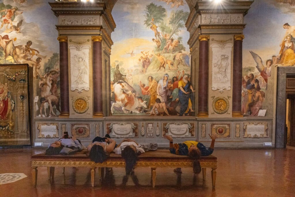 Three visitors lying on a bench to view Renaissance ceiling frescoes in a Florence chapel