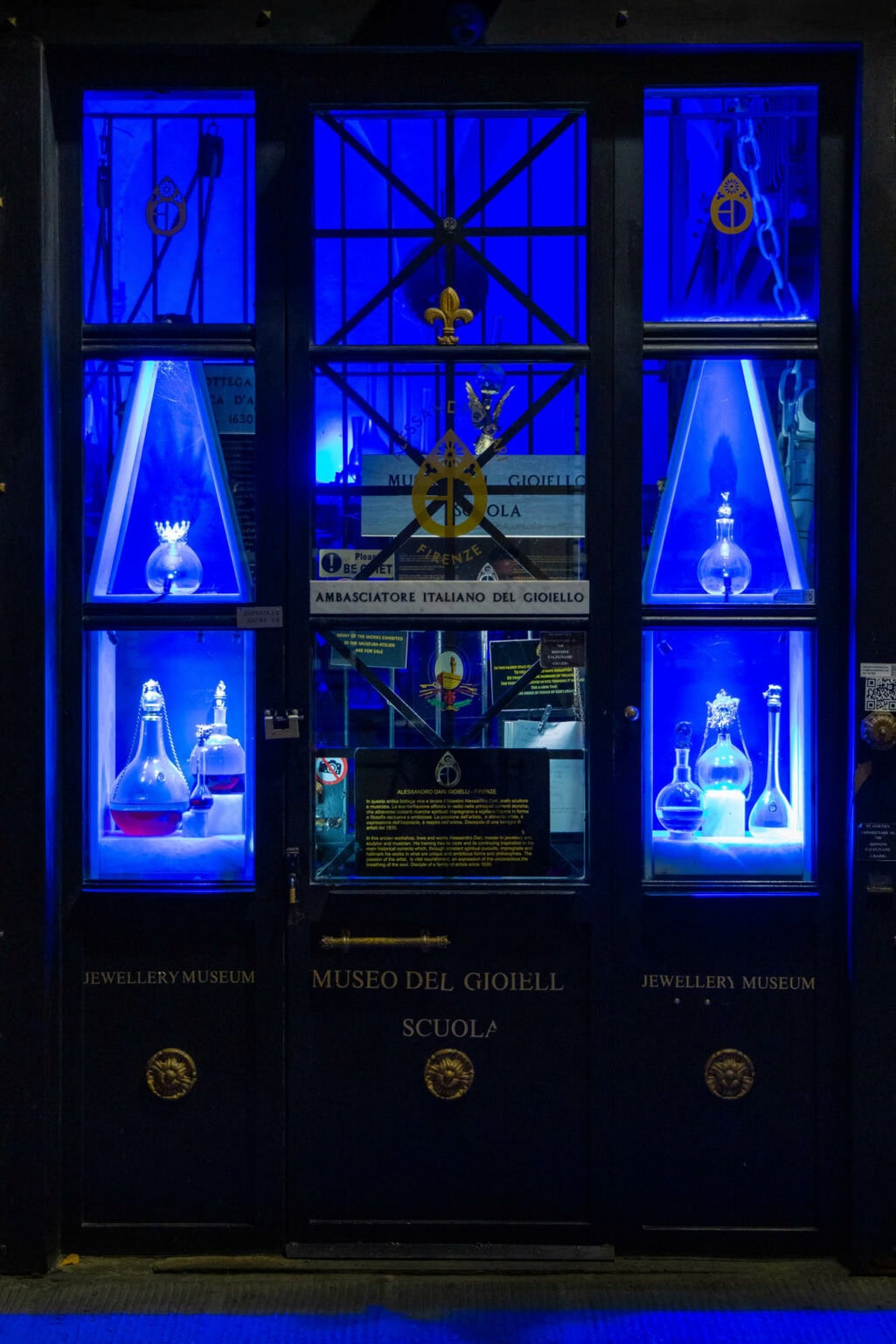 Illuminated museum display window featuring ornate blue-lit perfume bottles and decorative objects, Florence, Italy