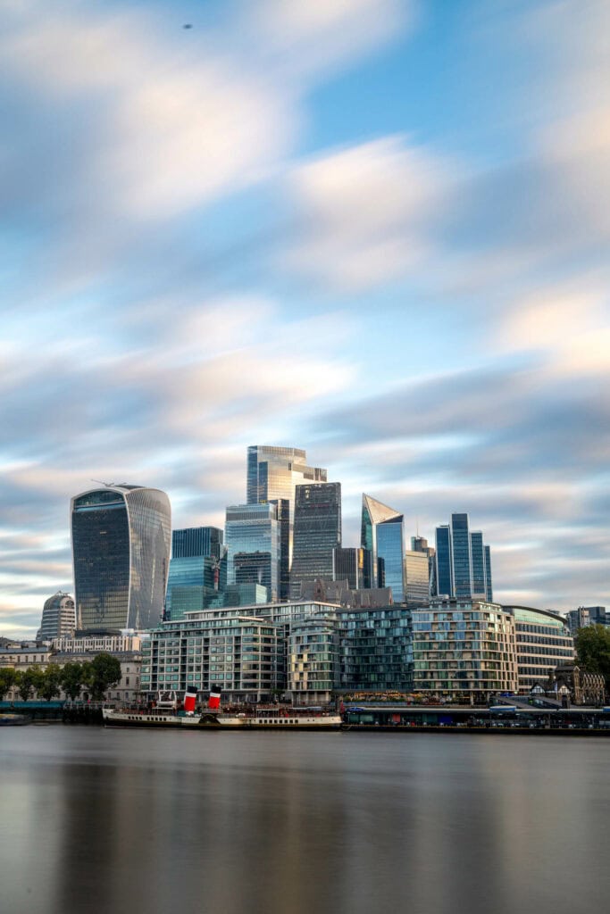 London skyline at dusk with modern skyscrapers reflected in the Thames, soft clouds and golden light
