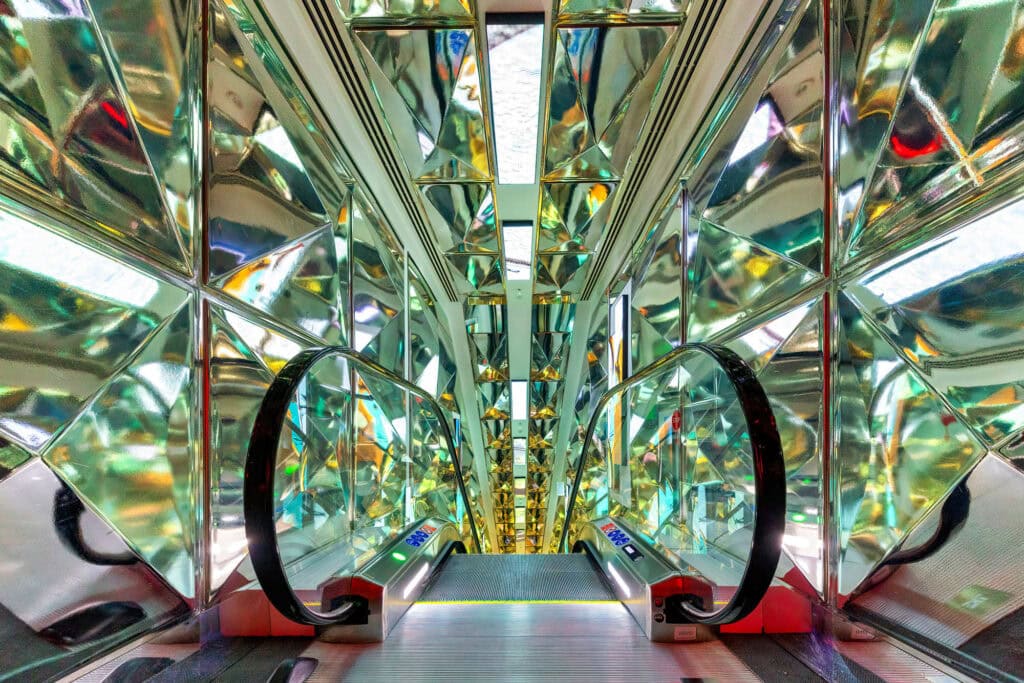 Symmetrical interior of a mirrored train car in Florence or London, with colorful reflections and geometric patterns stretching toward vanishing point