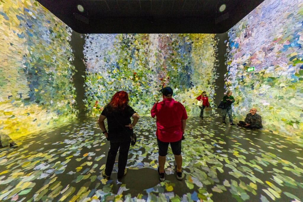 Visitors walking through the Frameless installation in London, colorful floral patterns projected across the walls and floor