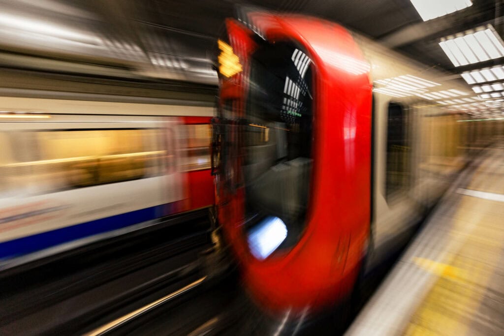 A red London Underground train pulling out of the station platform, motion blurred
