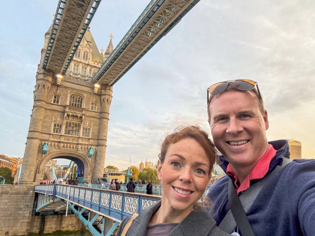 Smiling couple taking a selfie in front of Tower Bridge, London, at golden hour