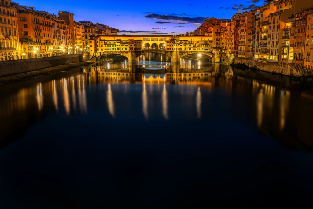 Ponte Vecchio after dark, lit windows and warm reflections on the still Arno