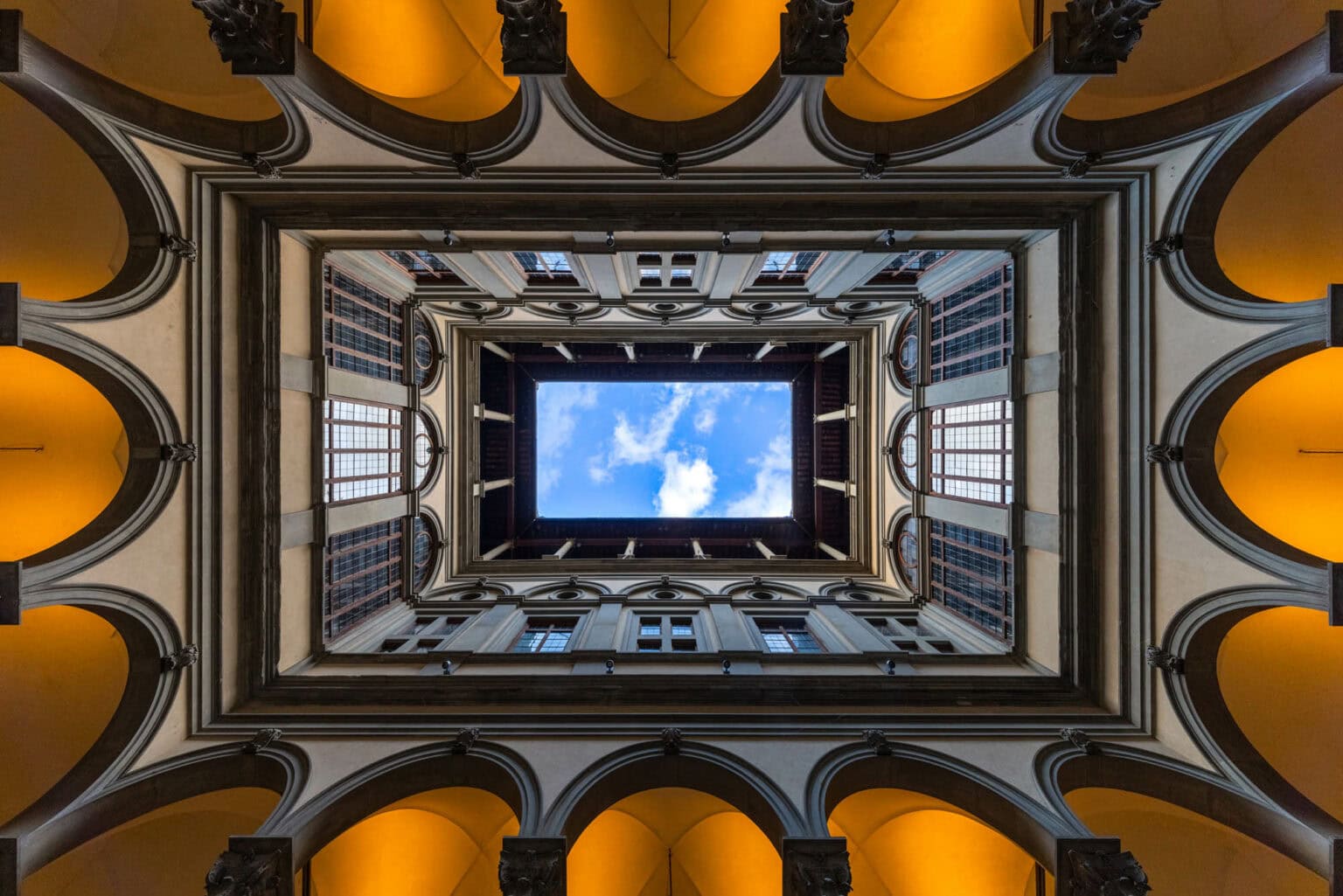 Looking up through a Florence courtyard, golden arches framing a rectangle of blue sky