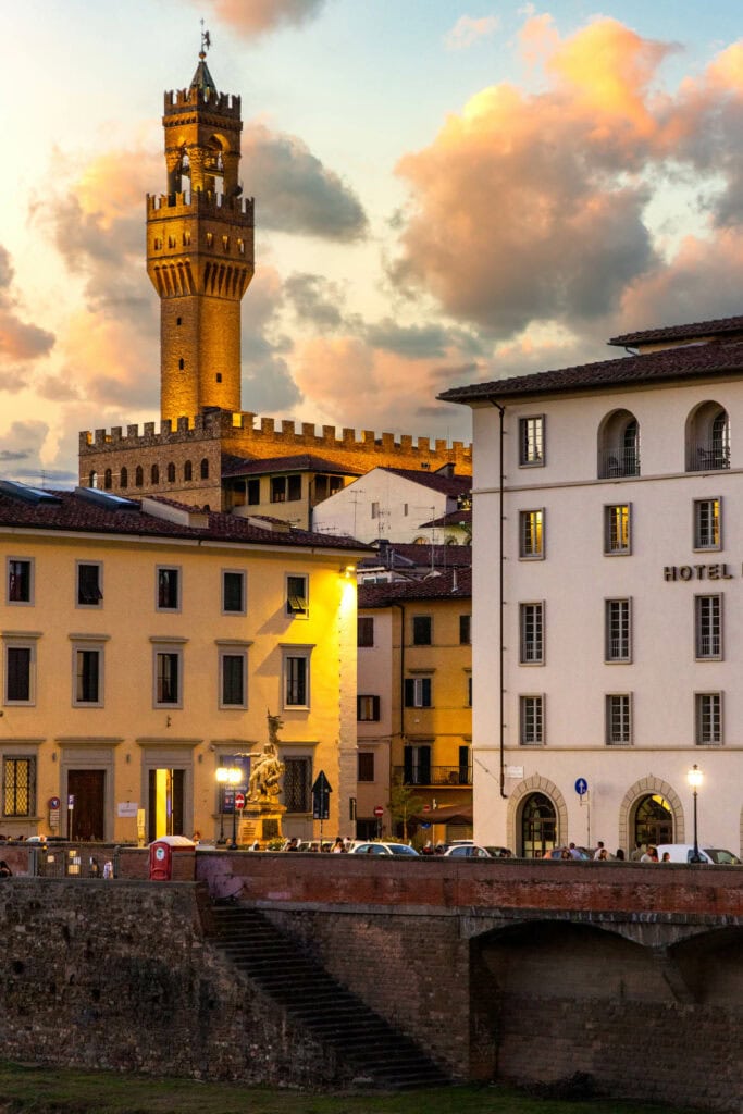 Palazzo Vecchio tower glowing gold at sunset above the Arno, seen from across the city
