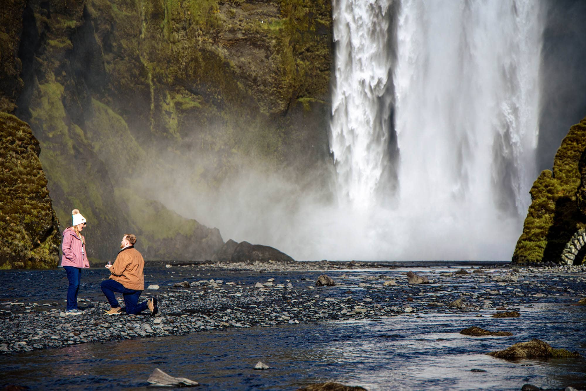 surprise proposal at Skógafoss waterfall, Iceland — couple embracing in the mist at the base of the falls