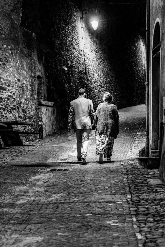 Two figures walking down a cobblestone European alley