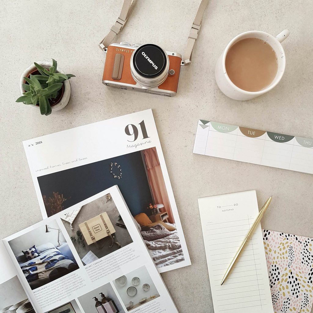 Styled flat lay with vintage camera, coffee cup, magazine, and stationery on neutral background
