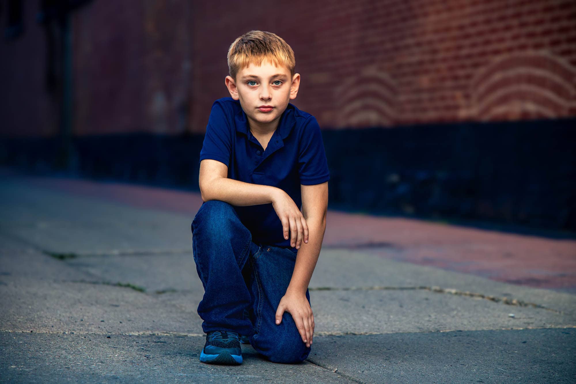 Boy crouched on a downtown sidewalk against a brick storefront