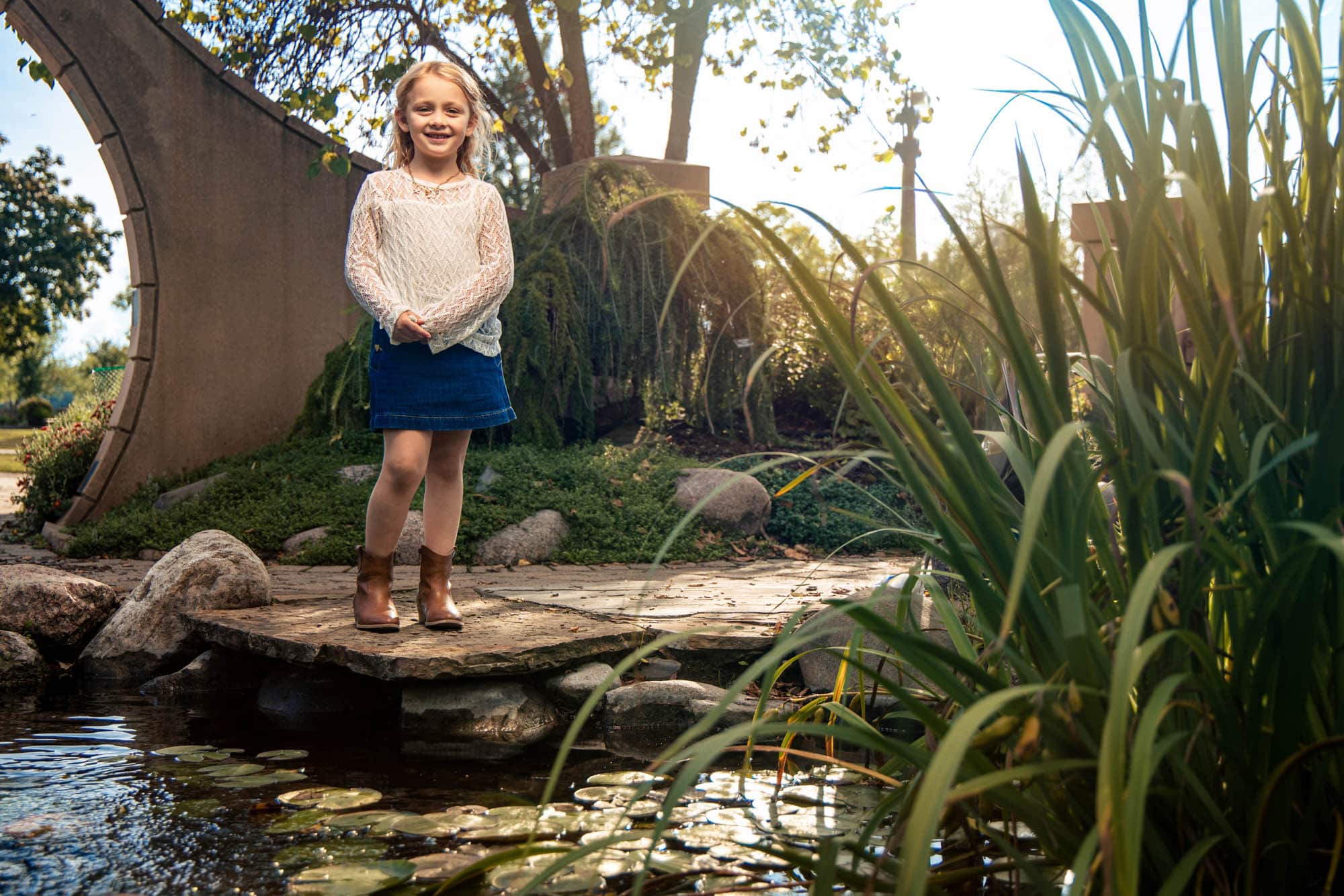 Girl standing on a stone path beside a garden pond with lily pads