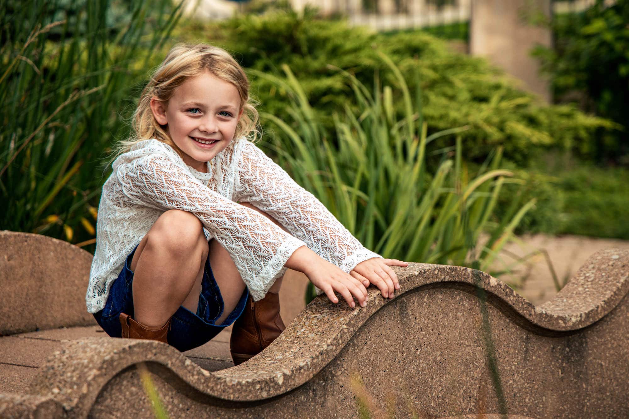 Young girl in a white lace top laughing while curled up on a curved stone bench