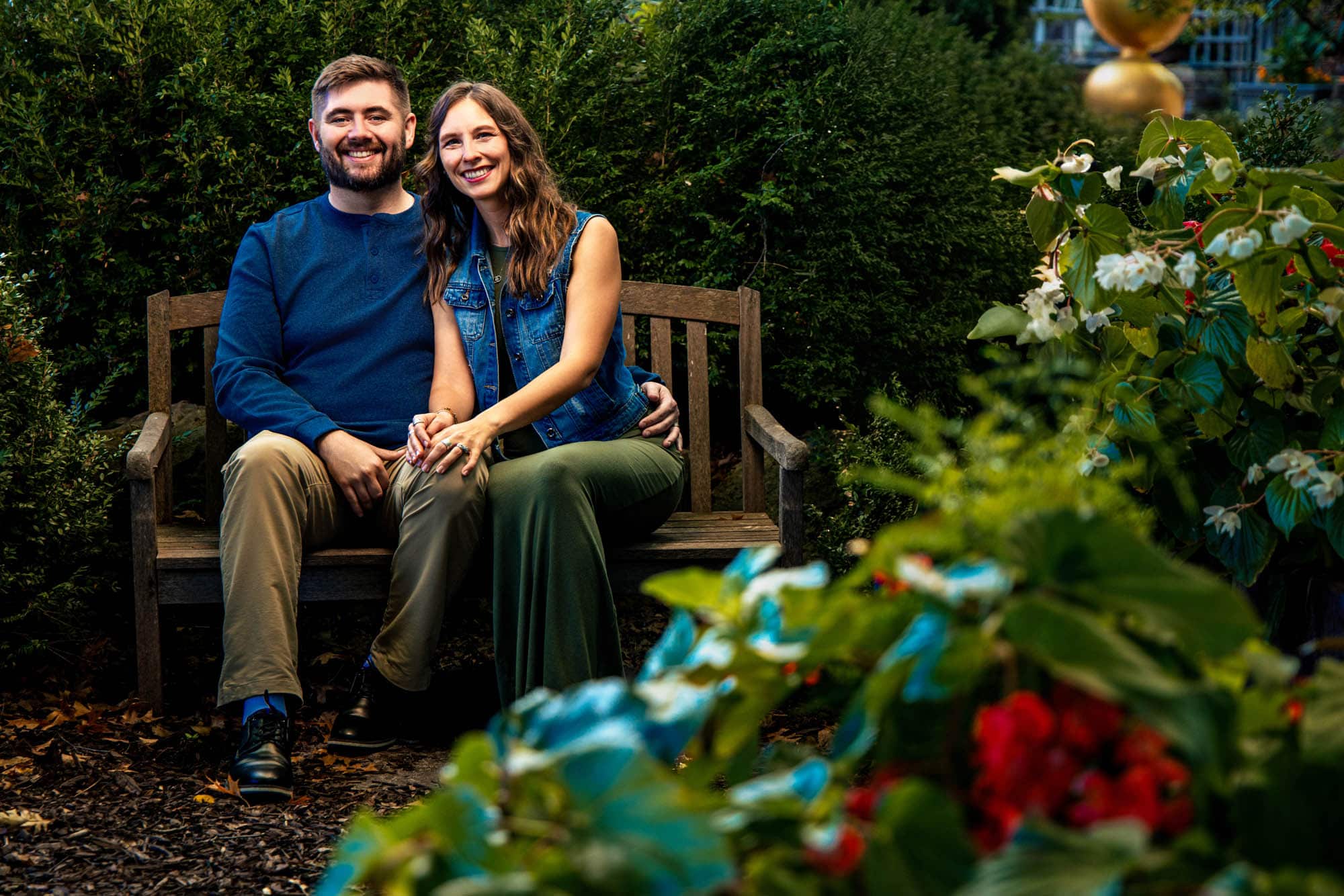 Mom and dad sitting together on a wooden bench surrounded by garden flowers