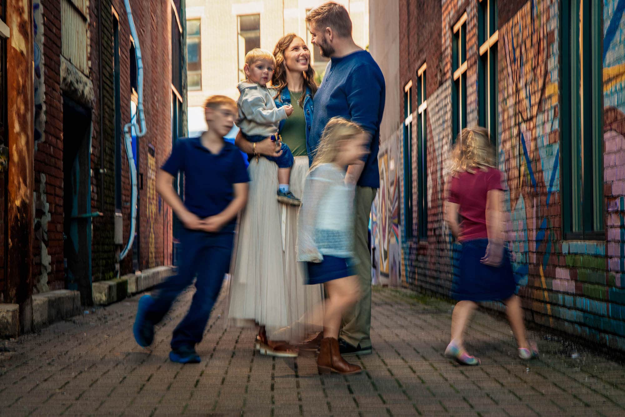 A family in a downtown La Crosse alley, the parents standing with their youngest while the kids run past