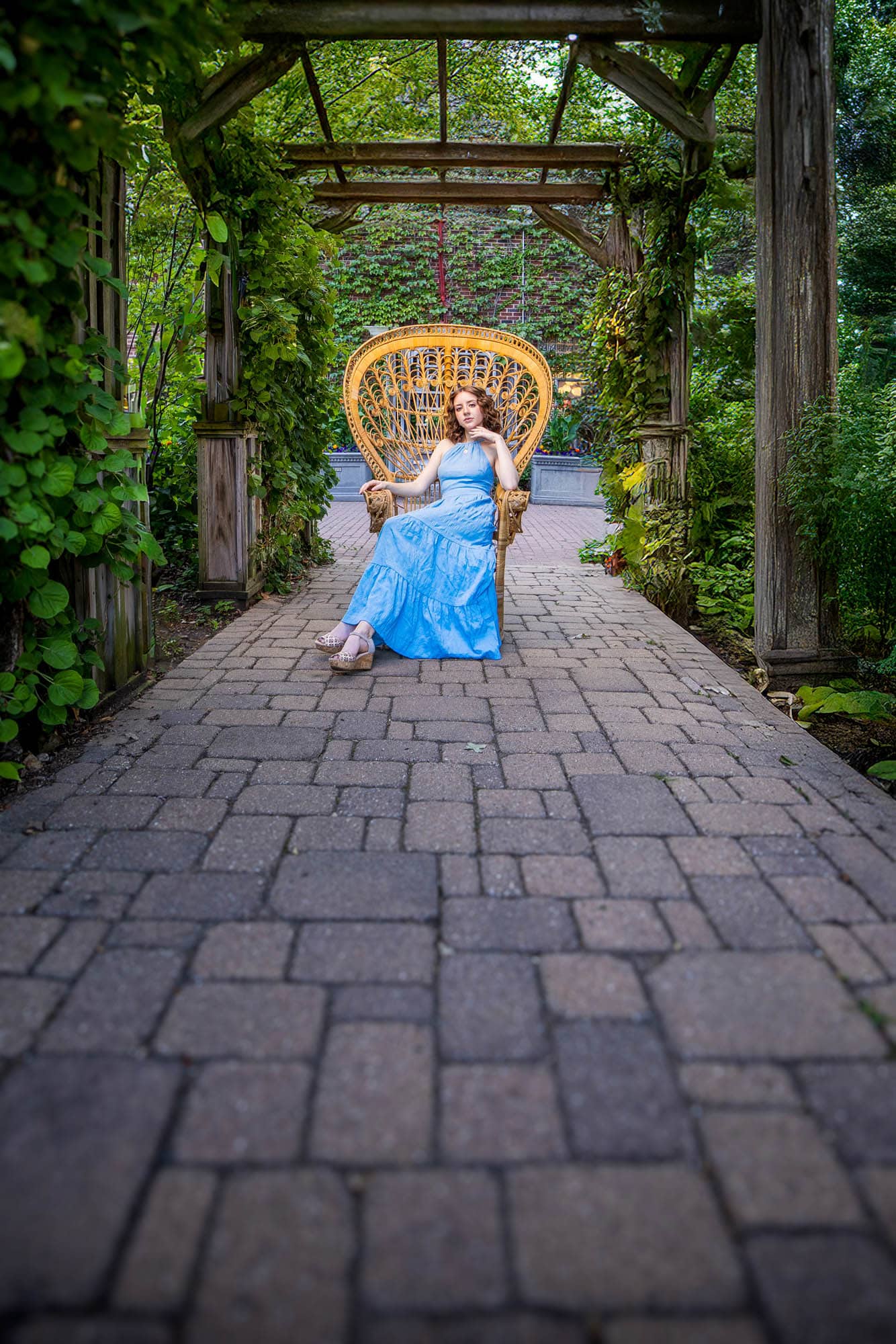 Ainsley seated in a wicker chair at the end of a garden pergola, Riverside International Friendship Gardens, La Crosse WI