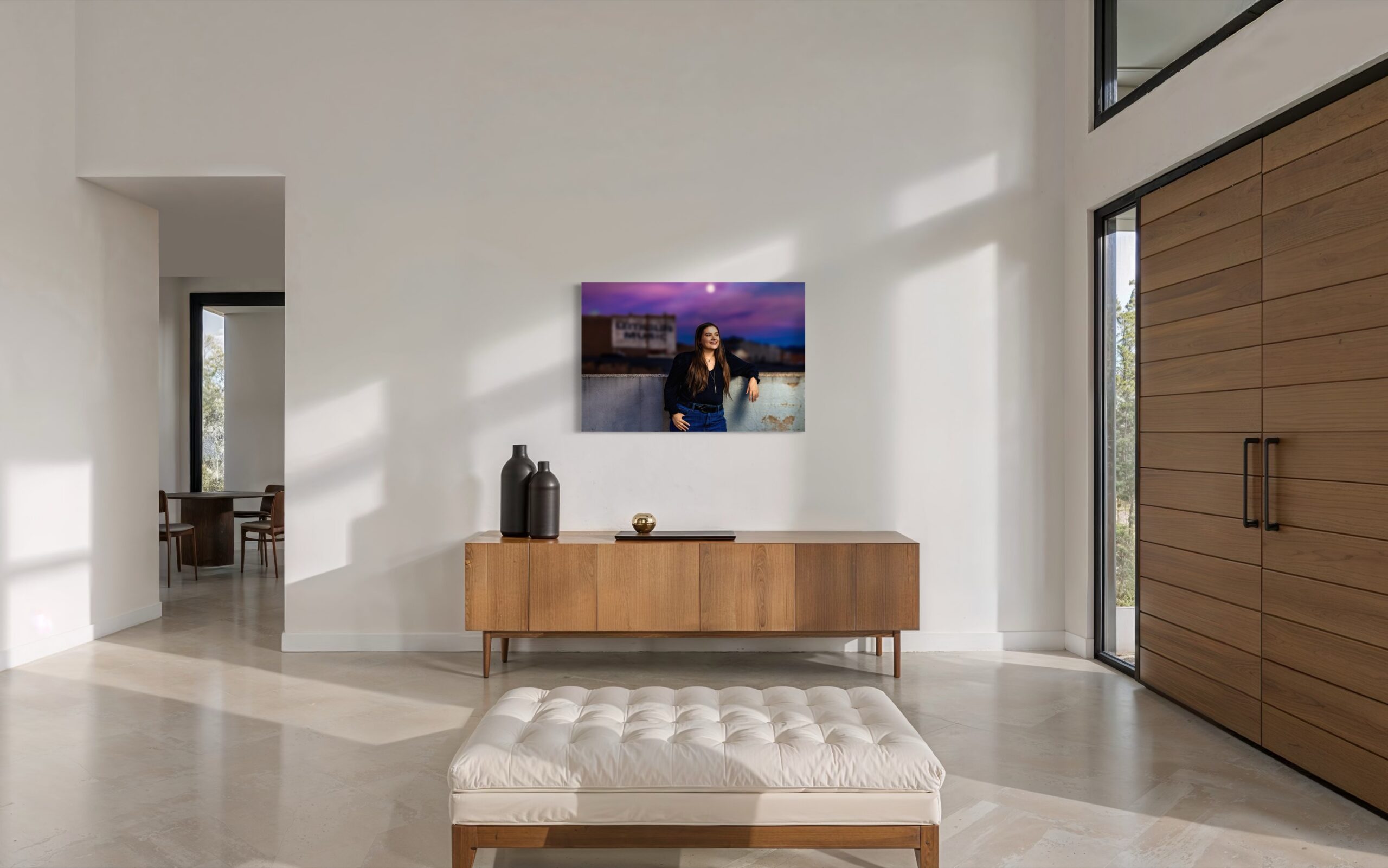 A large senior portrait of a student under a violet dusk sky, hung above a walnut sideboard