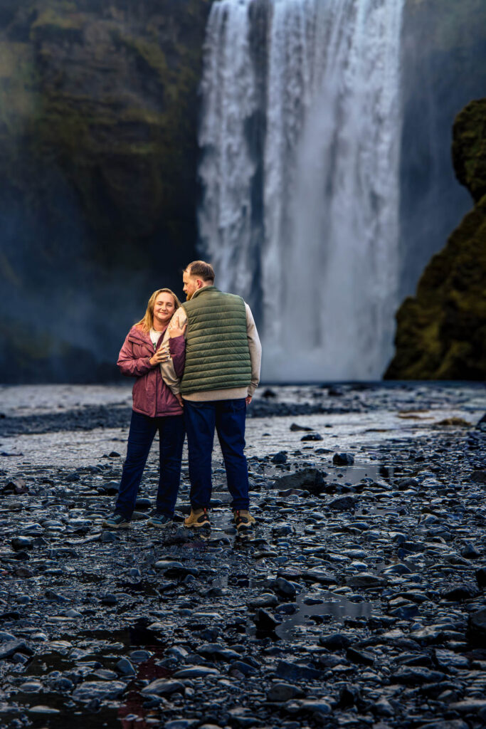 couple walking toward Skógafoss, glacial river in the foreground, falls in the distance