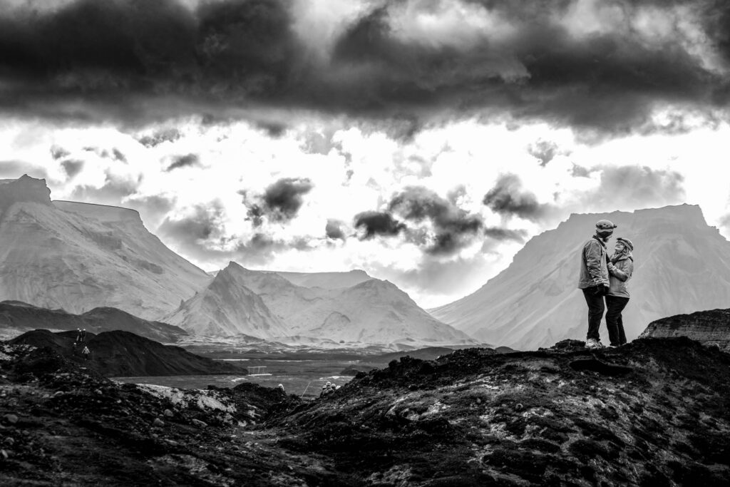 the moment of the proposal — one knee on the black volcanic rock, Skógafoss rushing behind them