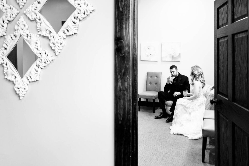 Black-and-white candid of bride and groom sitting together quietly in a waiting room before the ceremony