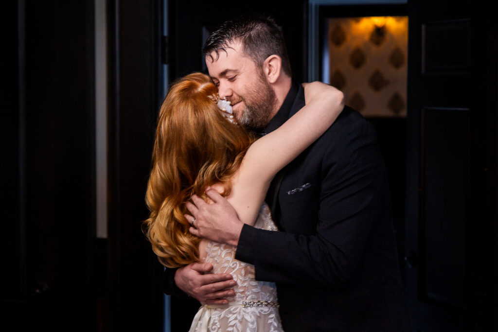 Groom in a black suit holding his bride in a tight, tearful embrace on the dance floor