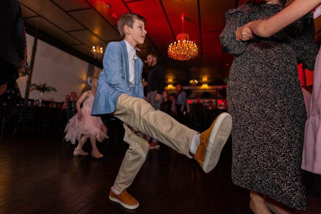 Boy in a blue blazer kicking his leg high on the wedding reception dance floor