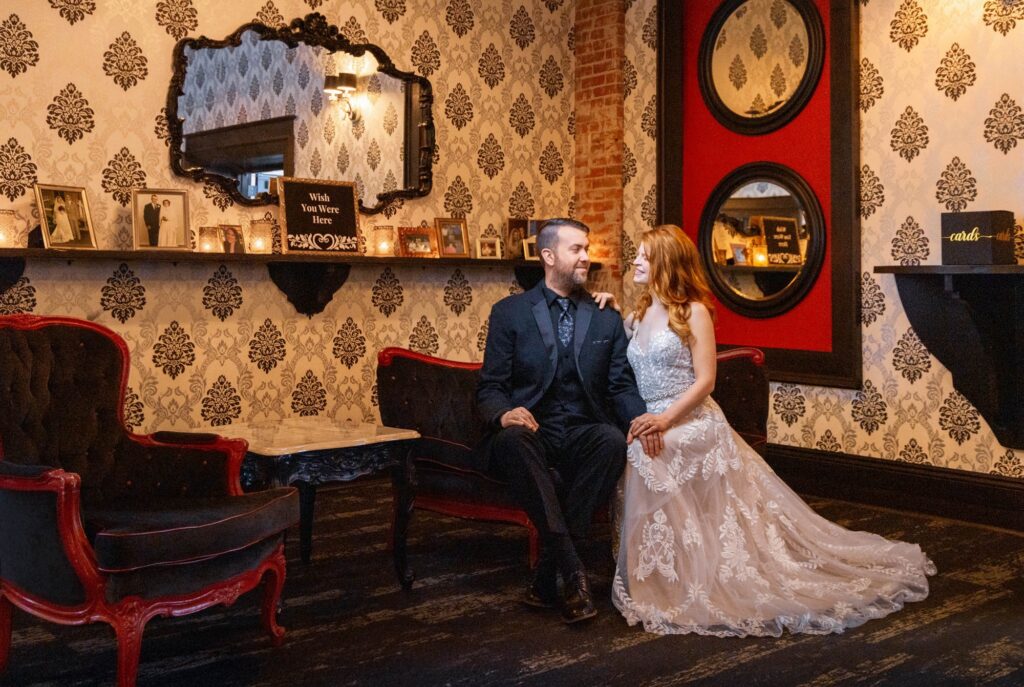 Bride and groom laughing together on a velvet settee beside ornate damask wallpaper