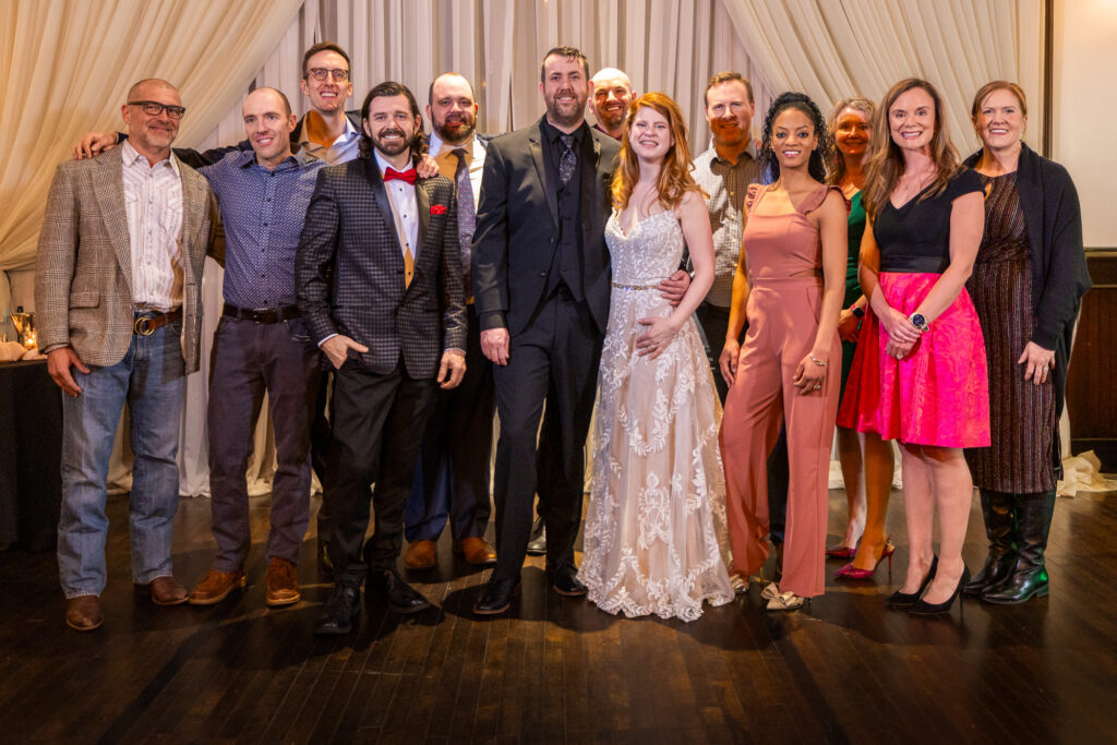 Bride and groom surrounded by a smiling group of twelve wedding guests on the dance floor