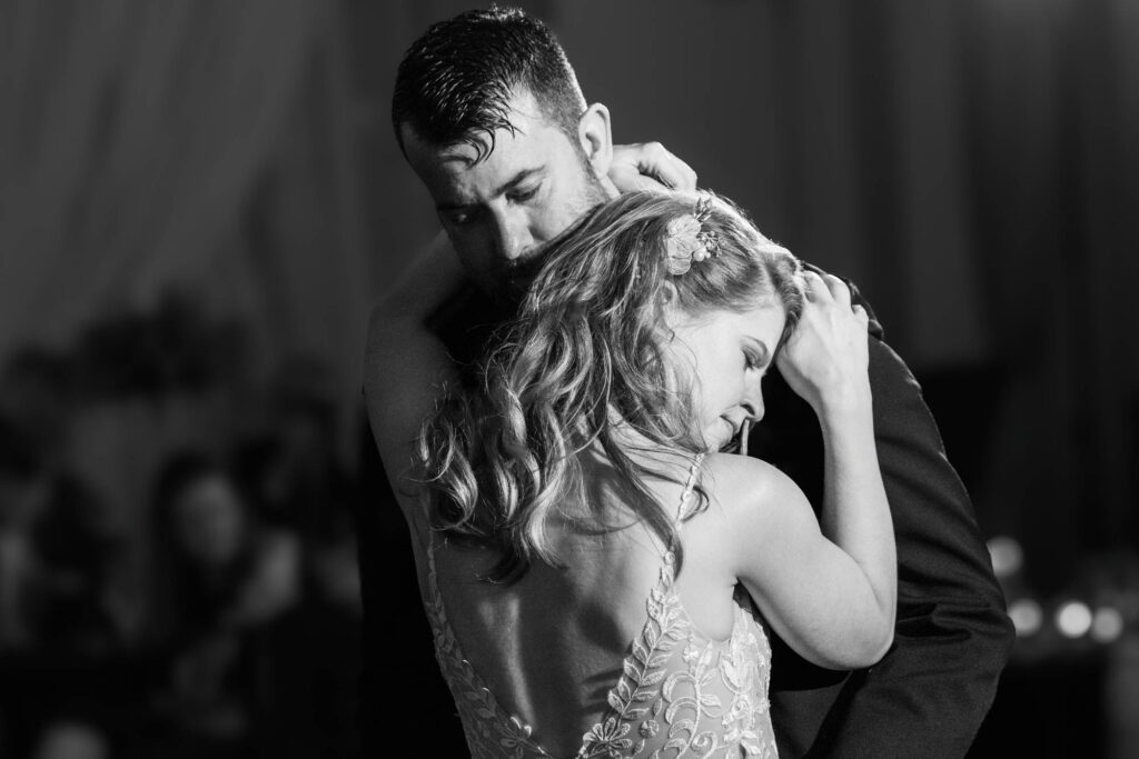 Black-and-white close-up of bride and groom holding each other cheek to cheek during their first dance